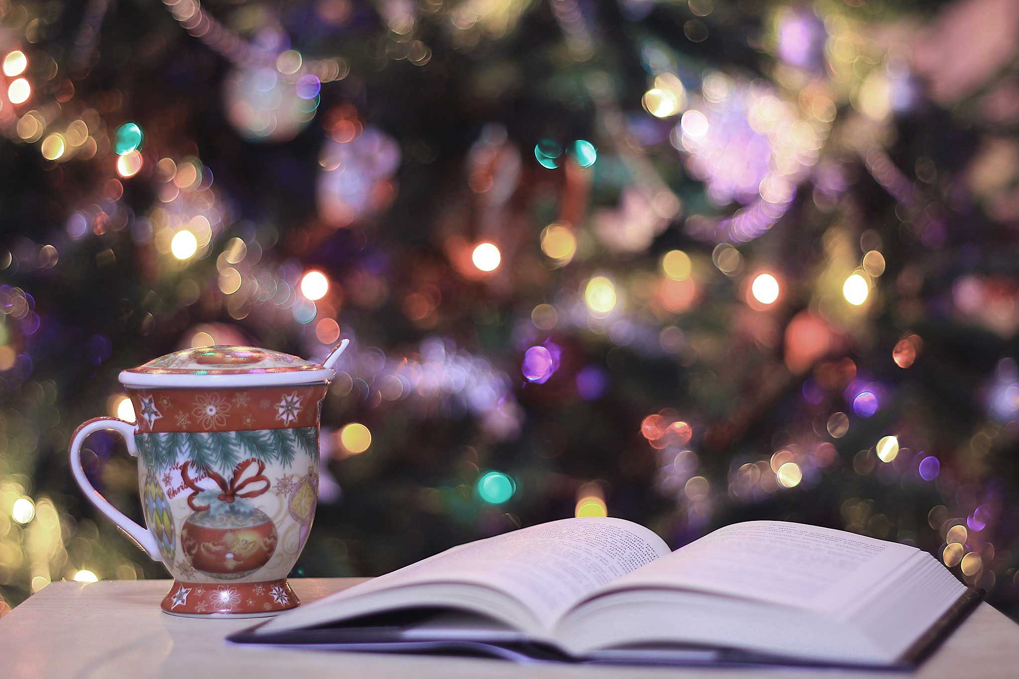 aufgeschlagenes Buch mit einer Weihnachtstasse vor einem Christbaum